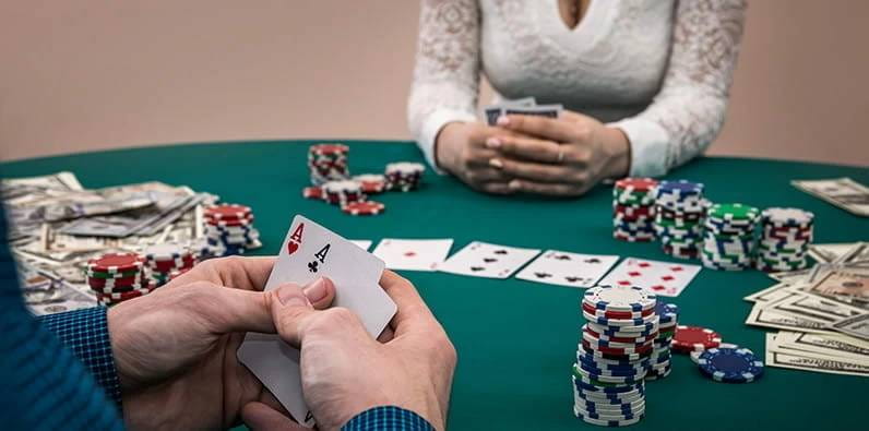 Une table de casino avec des cartes, des jetons et de l'argent en piles et un joueur avec deux as dans ses mains.