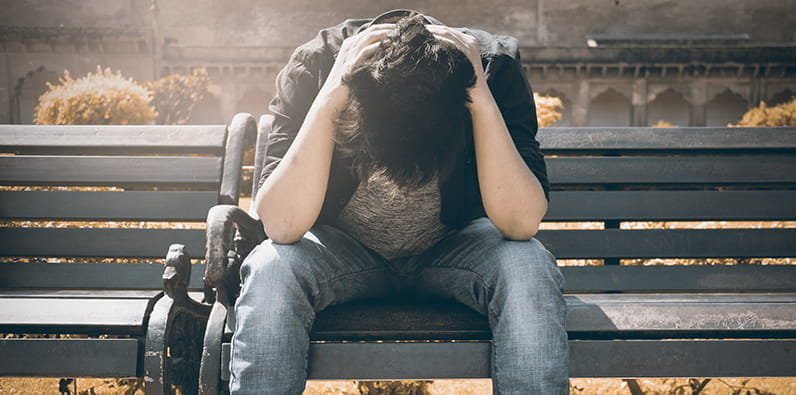 Un hombre sentado en un banco con las manos puestas en su cabeza 